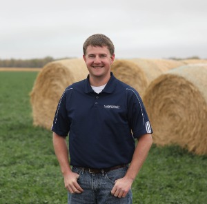 Joe Hickman standing in alfalfa field with hay bales behind him
