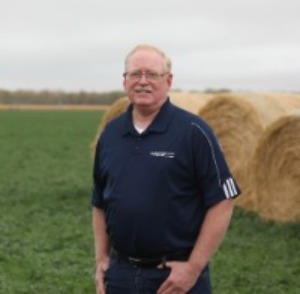 Bryan Trimble standing in alfalfa field with hay bales behind him
