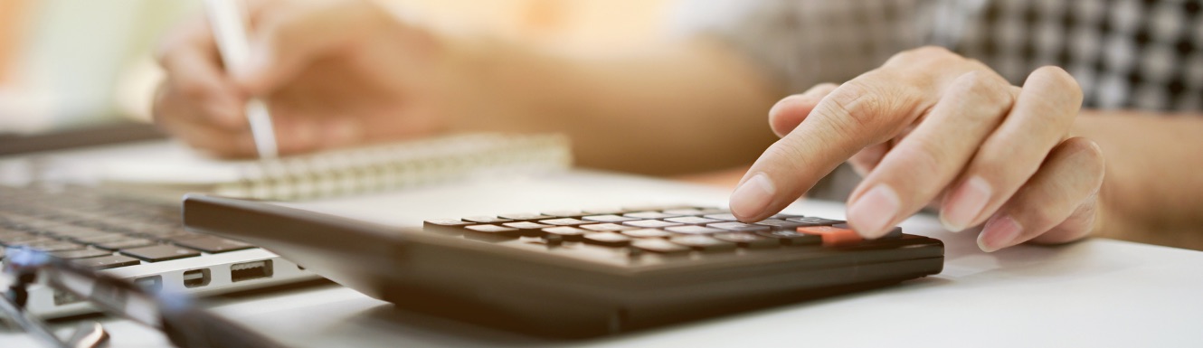 Image of a person using a calculator with one hand and writing notes with their other hand.