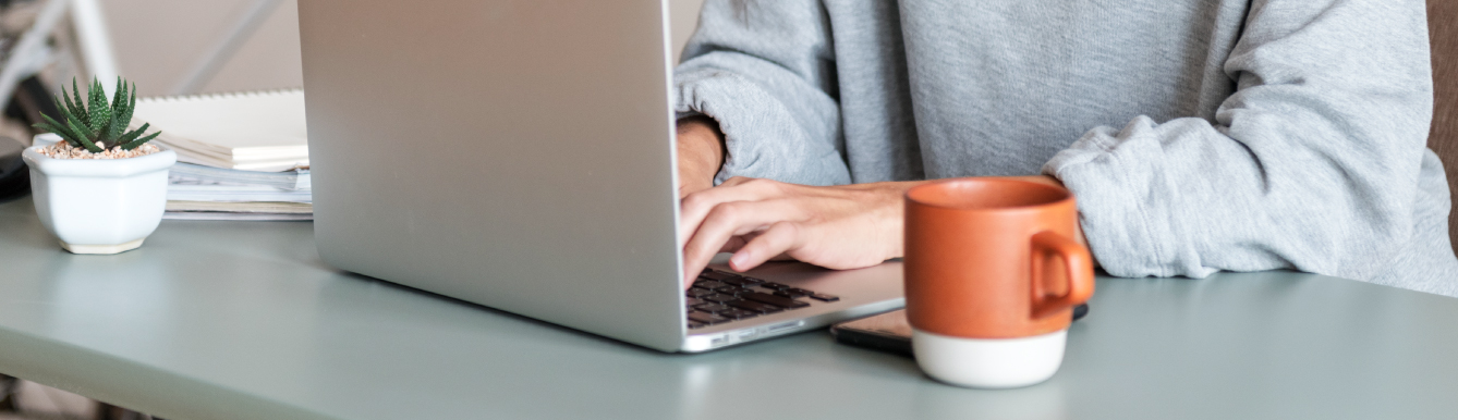 Woman typing on laptop with a red mug sitting next to her