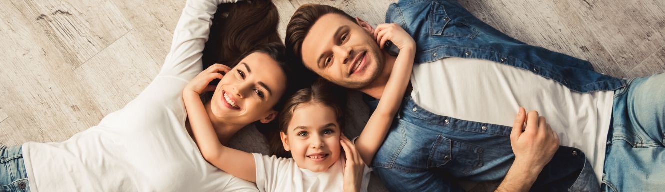 Dad, mom, and little girl laying on floor in a circle with their heads touching