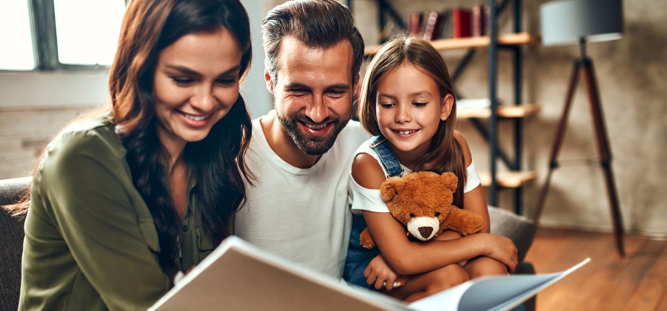 young family of three smiling while reading a story
