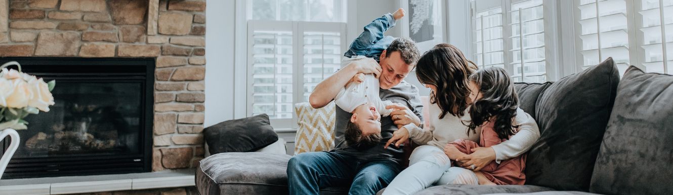 Two parents and two children playing on their living room couch in front of fireplace