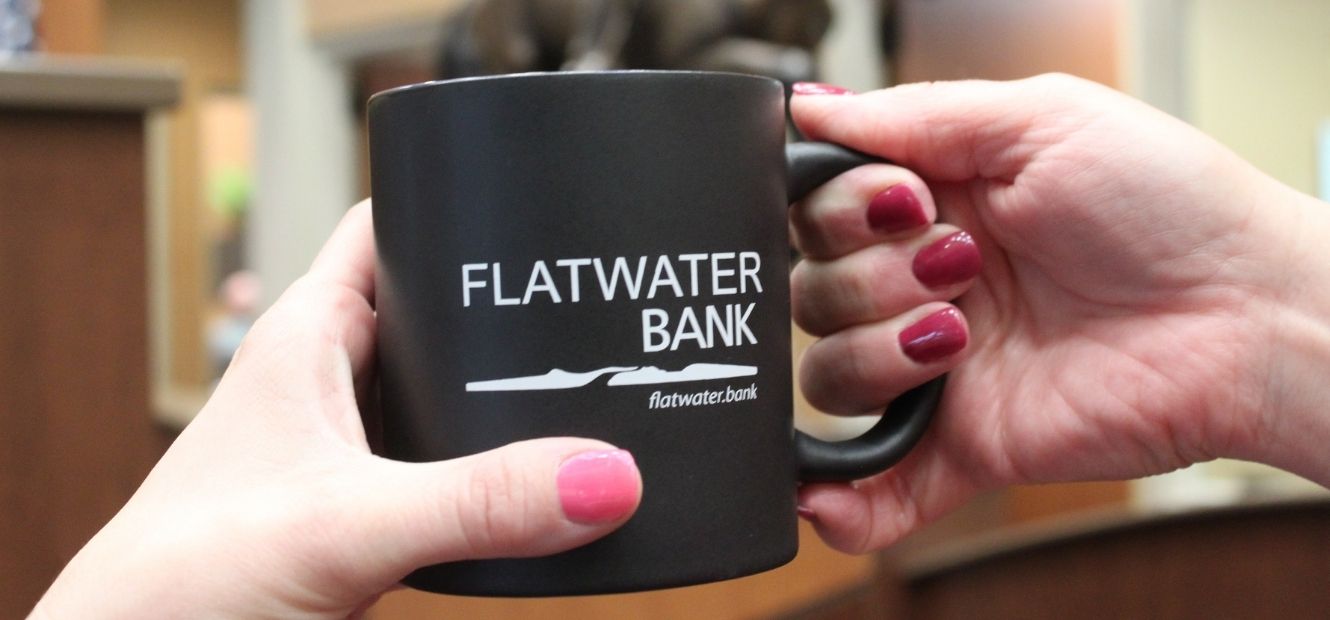 Flatwater Bank employee handing customer a mug with Flatwater Bank Logo
