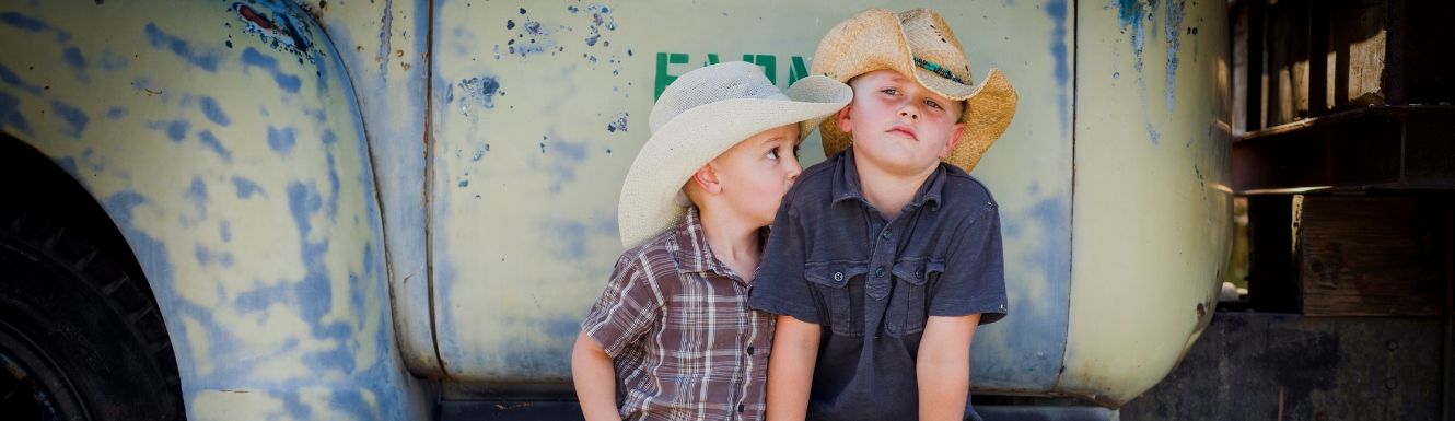Two little boys in cowboy hats leaning on running board of antique pick up truck