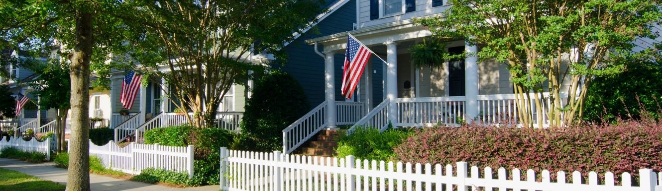 Two story home with American Flag displayed on patio with a white picket fence.