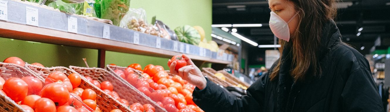 Woman in a face mask selecting tomato in grocery produce section