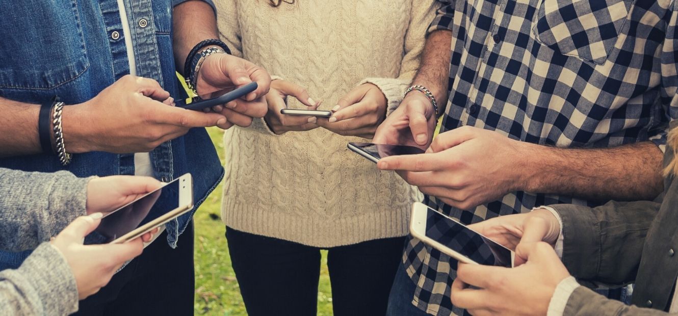 A group of friends standing in a circle holding their cell phones.
