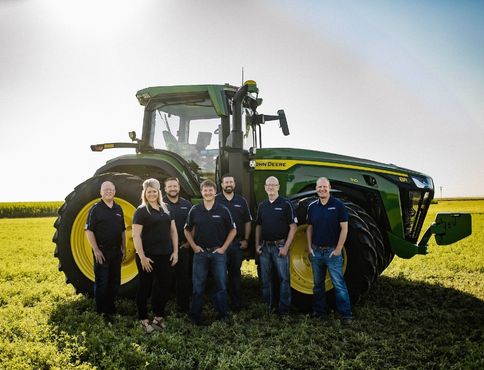 Flatwater Bank loan officers standing in front of green Tractor in a field. Left to Right: Bryan Trimble, Morgan Fornoff, Joe Libal, Joe Hickman, Bret Tiller, Monty Schriver, Ryan Groteluschen