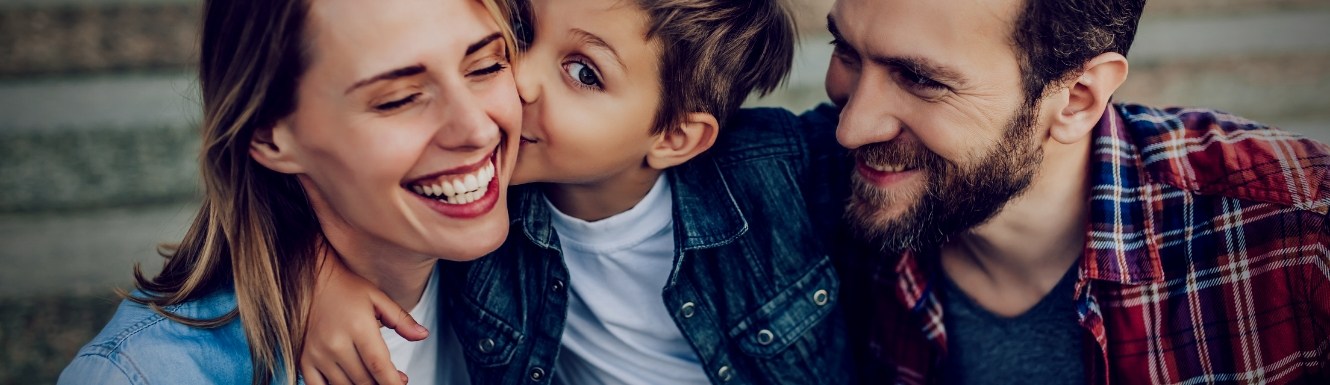 Woman and man holding little boy between them while boy kisses mothers cheek.