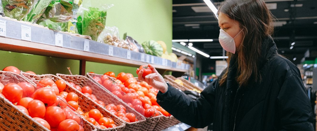 Woman in face mask shopping for tomatoes in grocery produce aisle