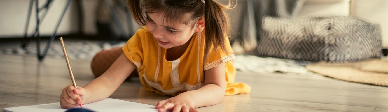 child laying on floor while writing in a notebook