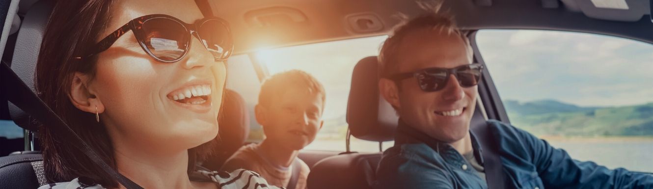 Smiling dad driving, mom in passenger seat with child in the back.